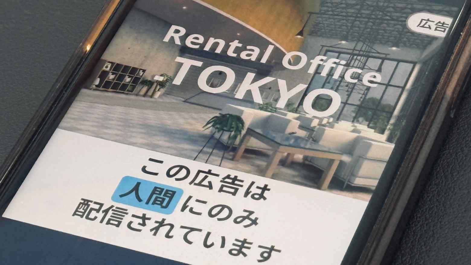A smartphone showing a Japanese ad with a label noting the ad is delivered to humans only