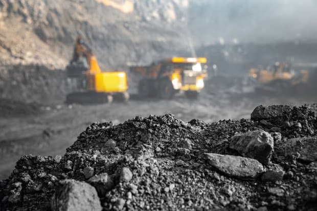 Heavy machinery working at an open pit coal mine with coal in the foreground