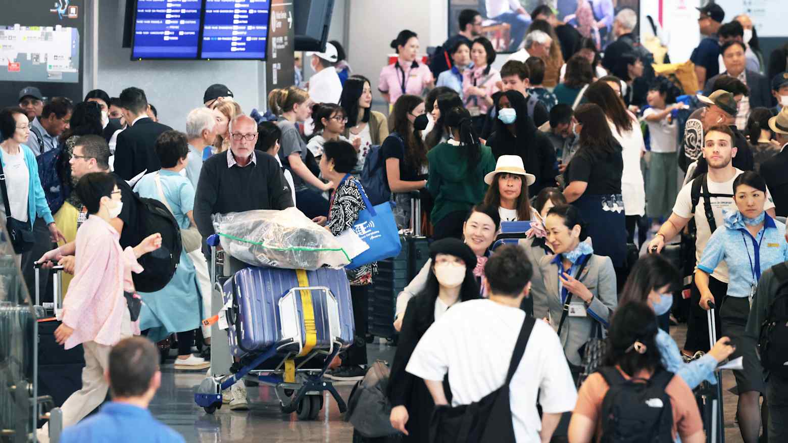Crowds of travelers with luggage fill a busy departure hall at a Japanese airport