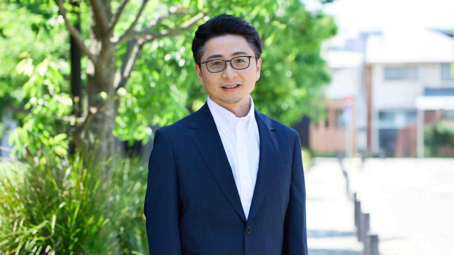 Oki Ito, Substack head of partnerships for Japan, standing outdoors in a dark suit beside a tree lined path