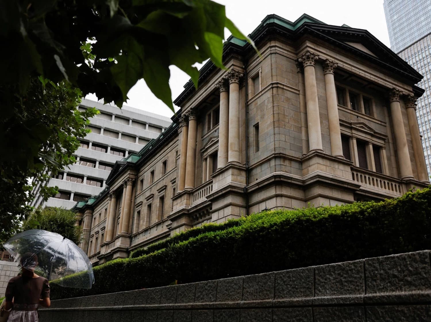 The Bank of Japan headquarters building in Tokyo with a pedestrian holding an umbrella in the foreground
