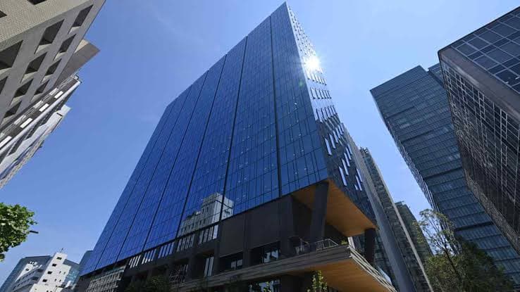A modern glass residential tower rises among high-rise buildings in a Japanese city