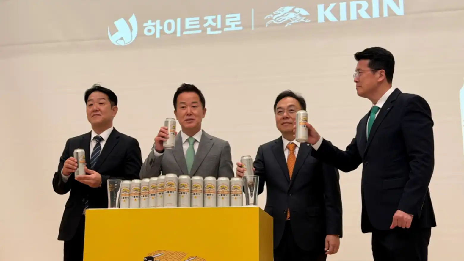 Executives from HiteJinro and Kirin raise cans of Ichiban Shibori beer on stage in front of both companies' logos