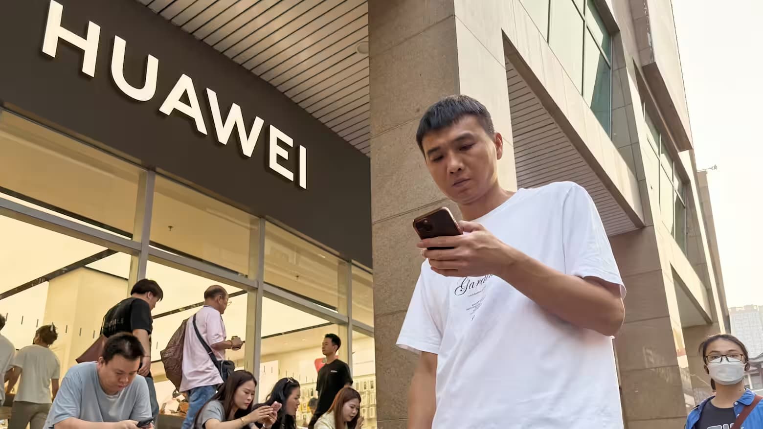 Shoppers gather outside a Huawei store in China as a man uses his smartphone