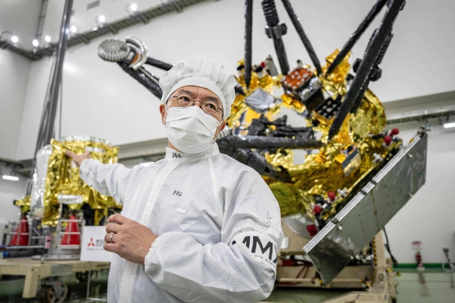 An engineer in a clean-room suit presents Japan's MMX spacecraft, wrapped in gold thermal foil, ahead of its mission to the Martian moon Phobos
