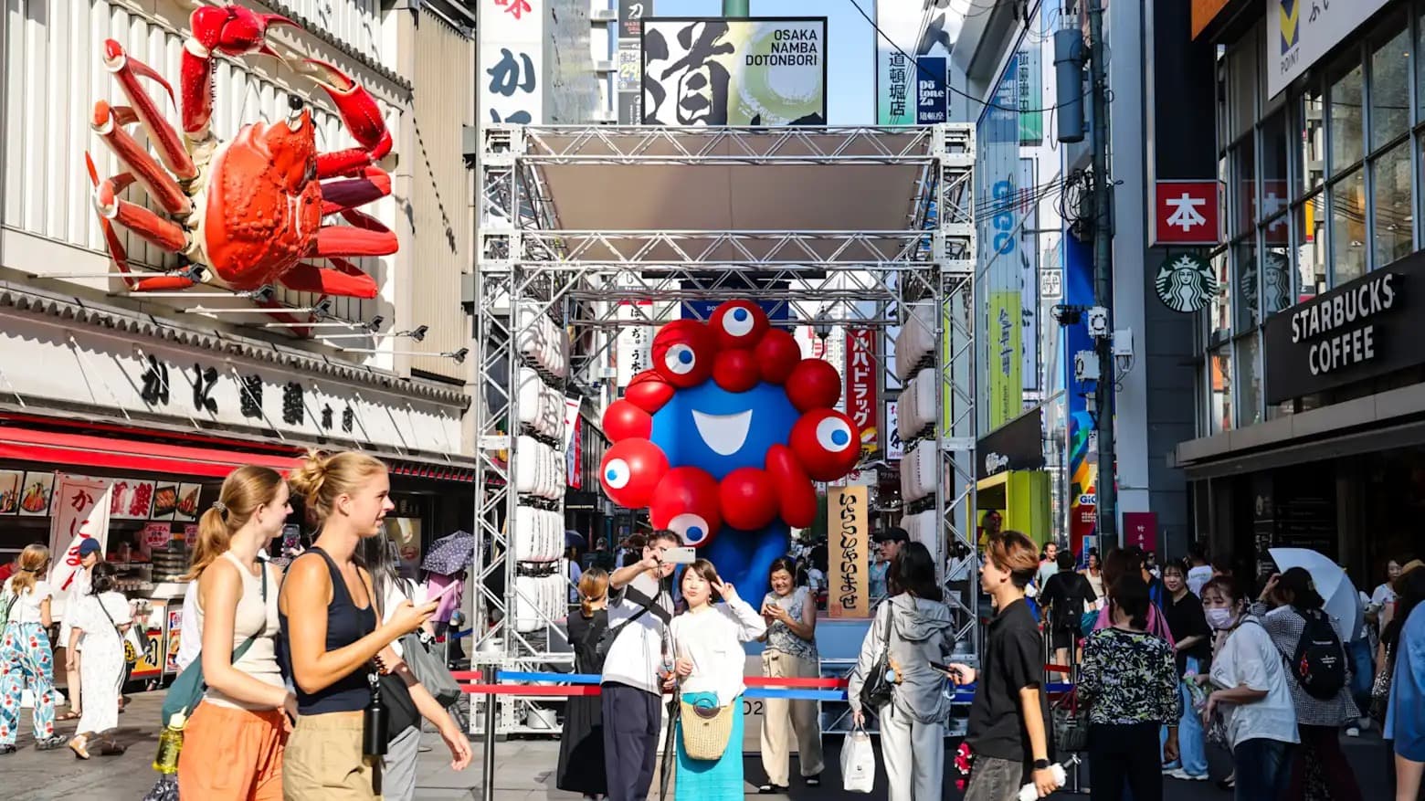 Tourists walking through the Dotonbori shopping district in Osaka beneath large crab and octopus signage