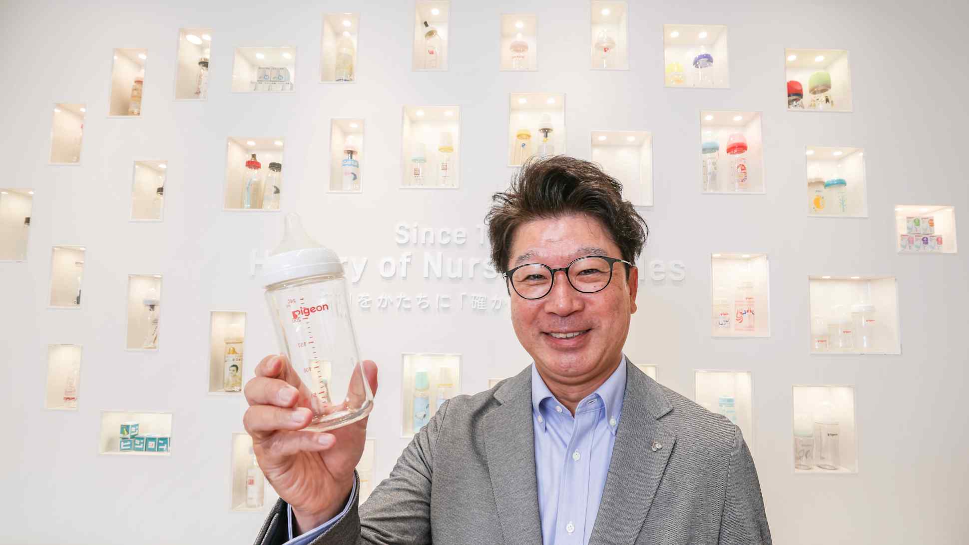 Pigeon Chief Executive Ryo Yano holds up a baby bottle in front of a wall displaying the company's historical nursing bottles