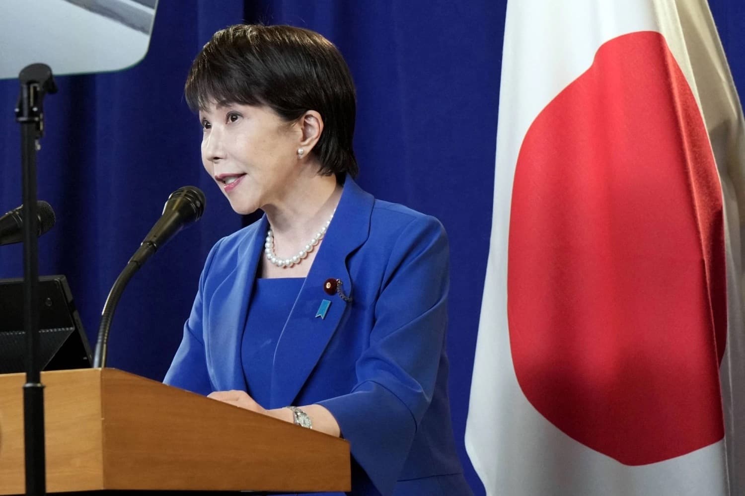 Japanese Prime Minister Sanae Takaichi speaking at a podium in front of a Japanese flag