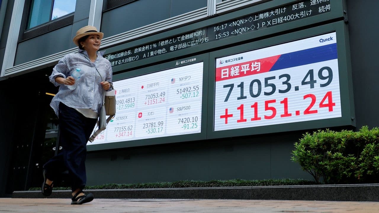 A pedestrian walks past an electronic board in Tokyo showing the Nikkei average and other global stock indexes