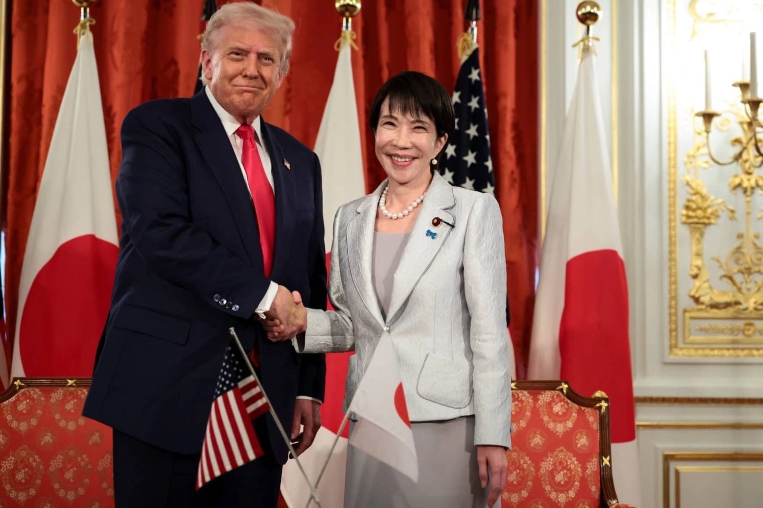 US President Donald Trump shaking hands with Japanese Prime Minister Sanae Takaichi in front of American and Japanese flags