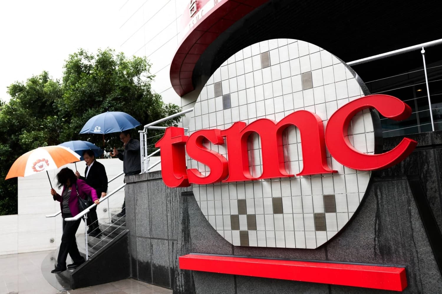 Pedestrians with umbrellas walk past the TSMC logo at a company building in Taiwan