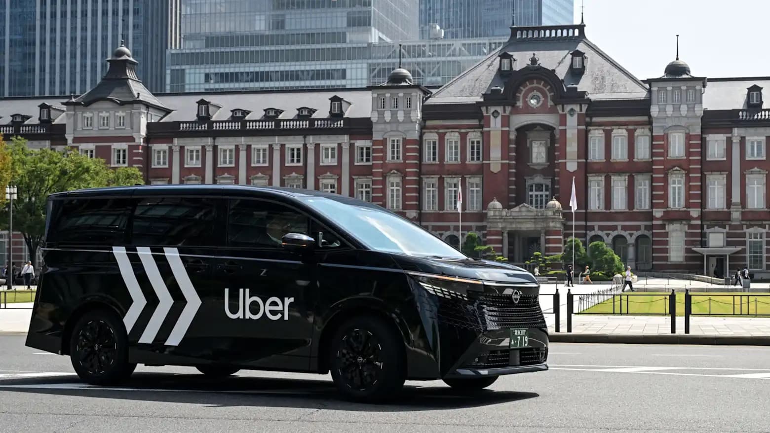 A black Nissan Elgrand minivan with Uber branding driving past Tokyo Station