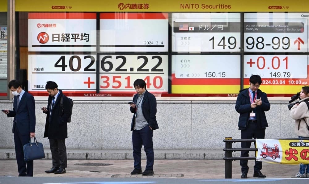 Pedestrians pass a stock market board in Tokyo showing the Nikkei index