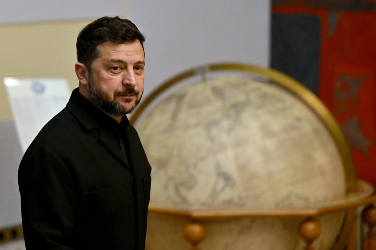 Ukrainian President Volodymyr Zelenskyy stands beside an antique globe